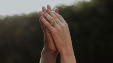 Two raised hands pressed together with wedding rings