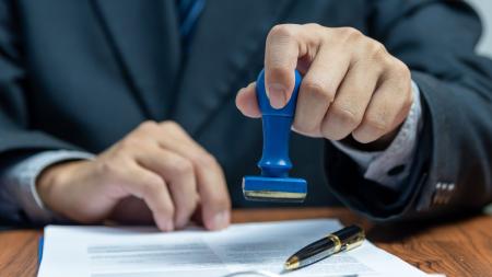 Person stamping a white piece of paper with text and a pen on top of it